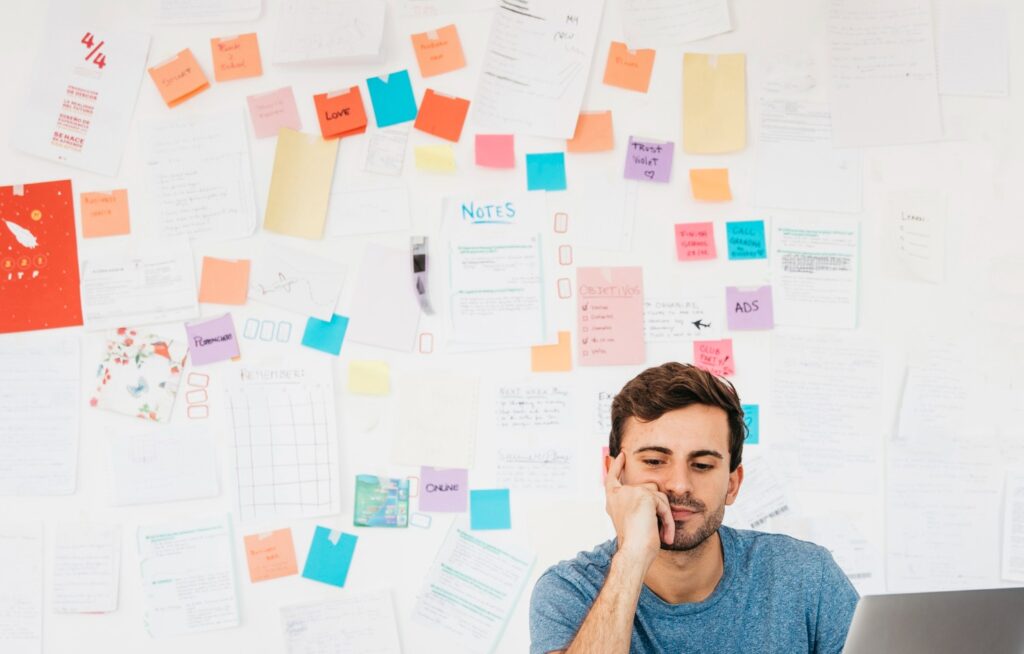 Hombre sentado hace un ejercicio de reflexión sobre sus actividades semanales, como parte de los consejos para ser productivo. A espaldas tienen múltiples notas de colores.