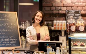Emprendedora sonriente en su cafetería, muestra una actitud de confianza tras aplicar una buena gestión y administración en su Pyme.