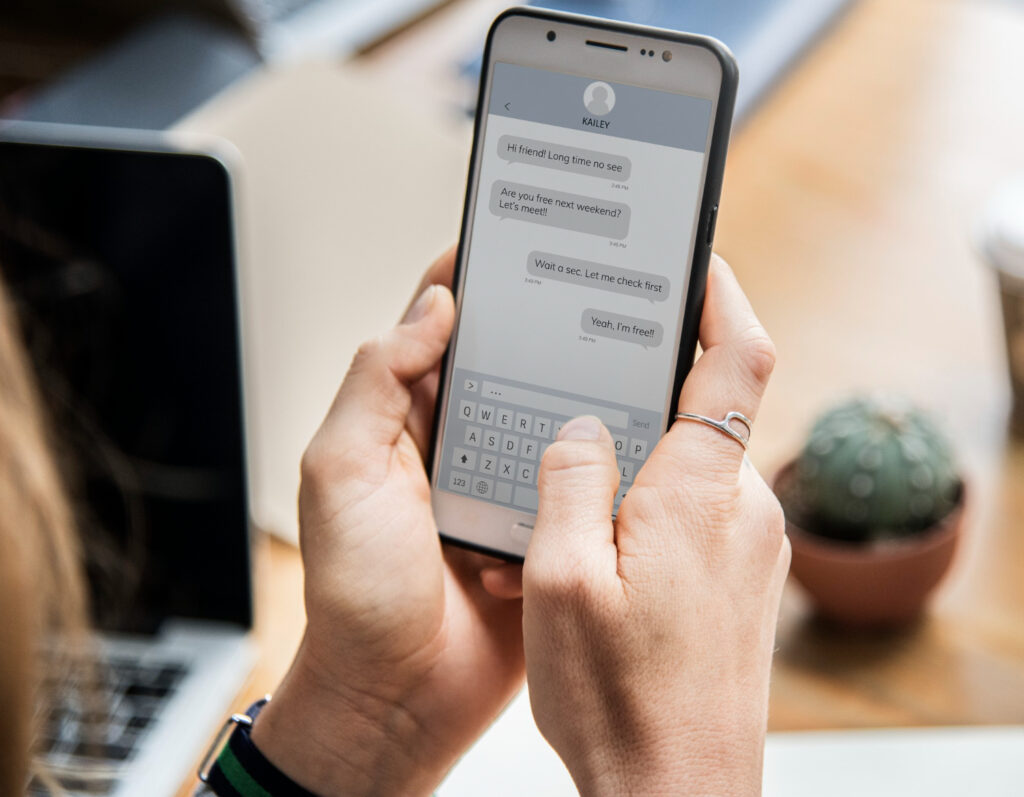 Las manos de una persona sostienen un teléfono celular en el que se ve una conversación por un app de mensajería tipo WhatsApp.