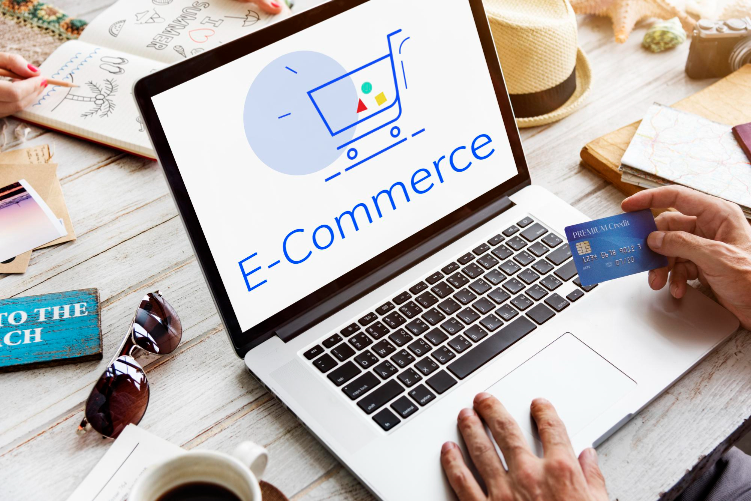 Vista de una computadora portátil sobre un escritorio. Sobre ellas hay unas manos con una tarjeta bancaria para ilustrar compras en un ecommerce.