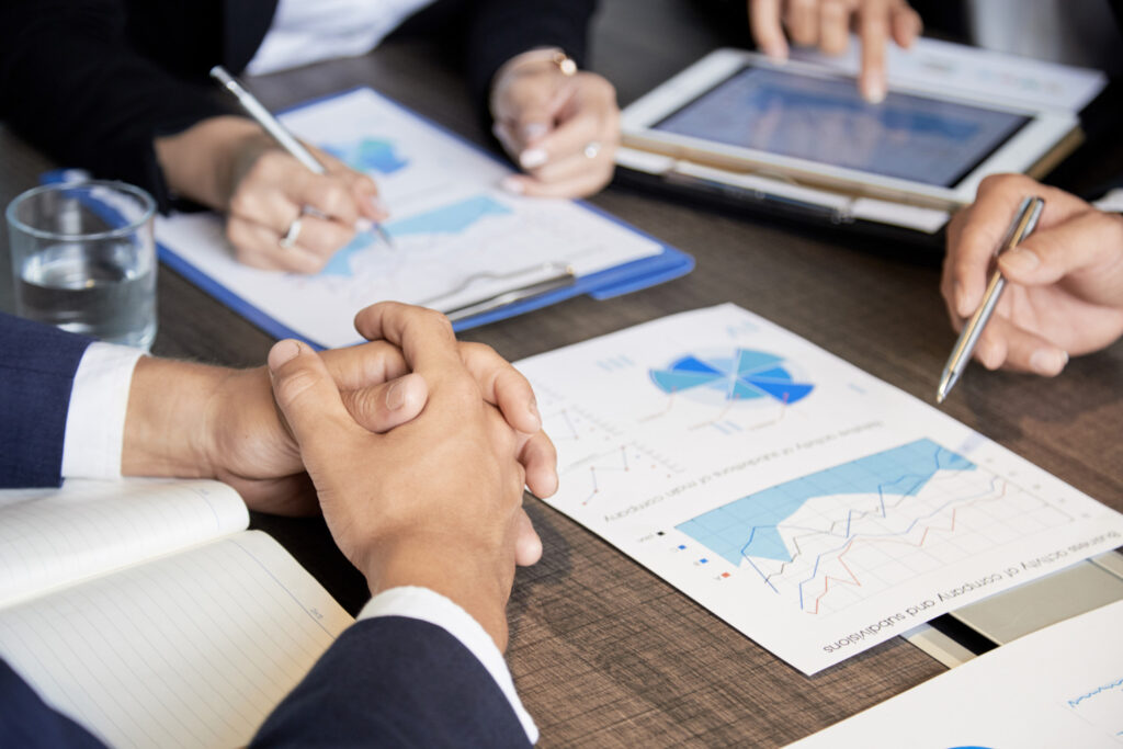 Vista de gráficas impresas y en una tableta electrónica, en una sesión de consultoría empresarial, donde están reunidas varias personas.