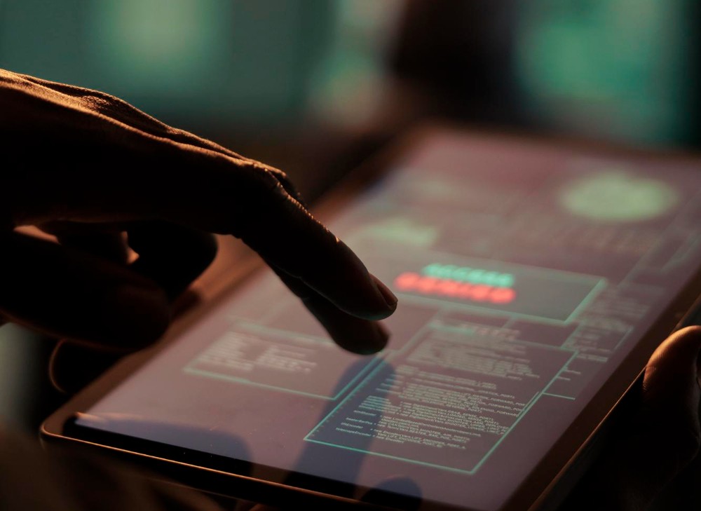 Persona utilizando una tableta con una pantalla que muestra datos y advertencias de seguridad digital, representando conceptos de ciberseguridad y protección de información.