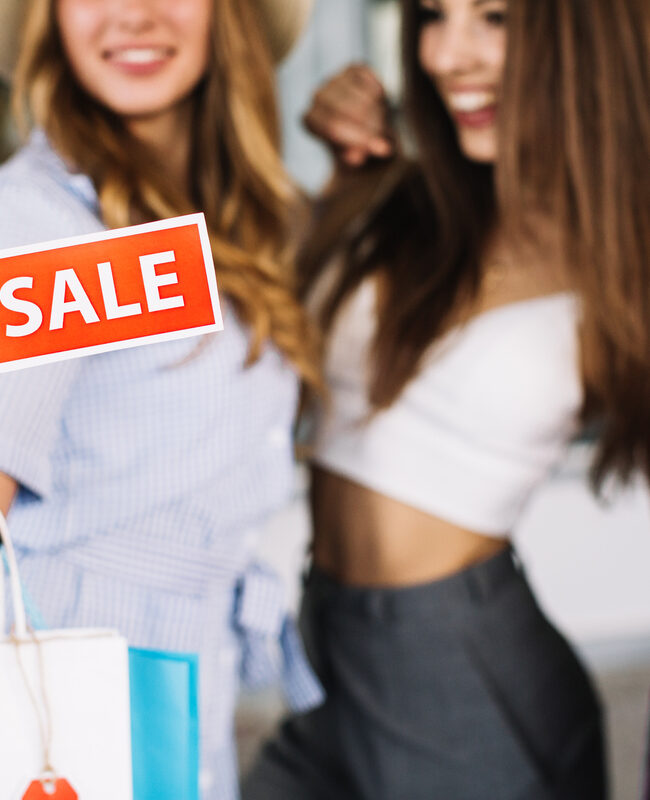 Mujeres jóvenes con bolsas de compra muestran una etiqueta con la palabra "sale".