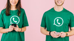 Vista parcial de dos personas que tienen playeras con el logo de WhatsApp y envían mensajes con su téléfono celular.