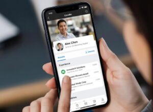 Vista de una mano que sostiene un teléfono celular donde se ve un perfil de LinkedIn