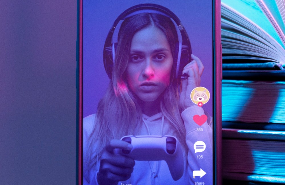 Close up de una pantalla de celular donde se ve una mujer con una consola de videojuegos en la mano.