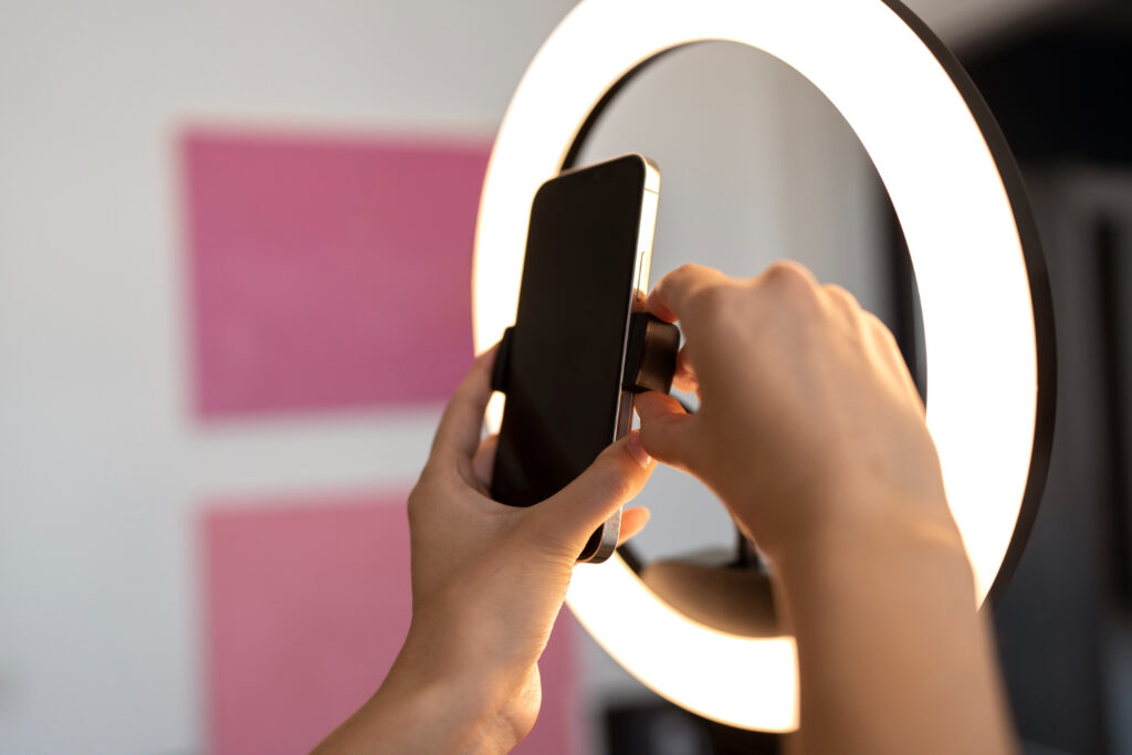 Vista de las manos de una persona que coloca un teléfono celular en un aro de luz utilizado para grabar videos para redes sociales.