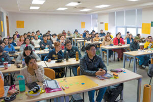 Vista de un aula con alumnos sentados en posición de poner atención a la clase que se imparte