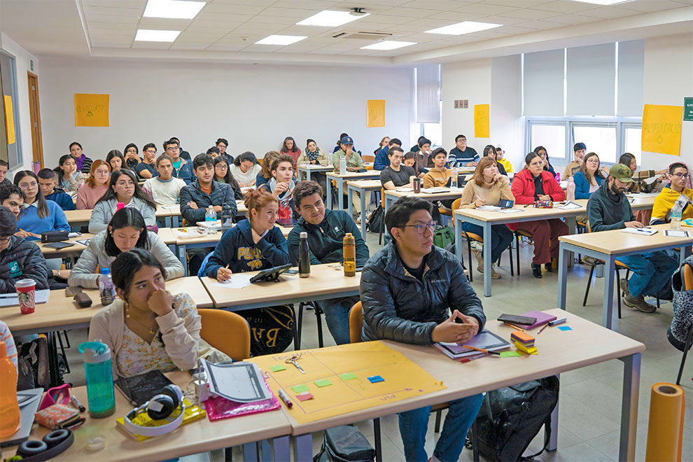 Vista de un aula con alumnos sentados en posición de poner atención a la clase que se imparte