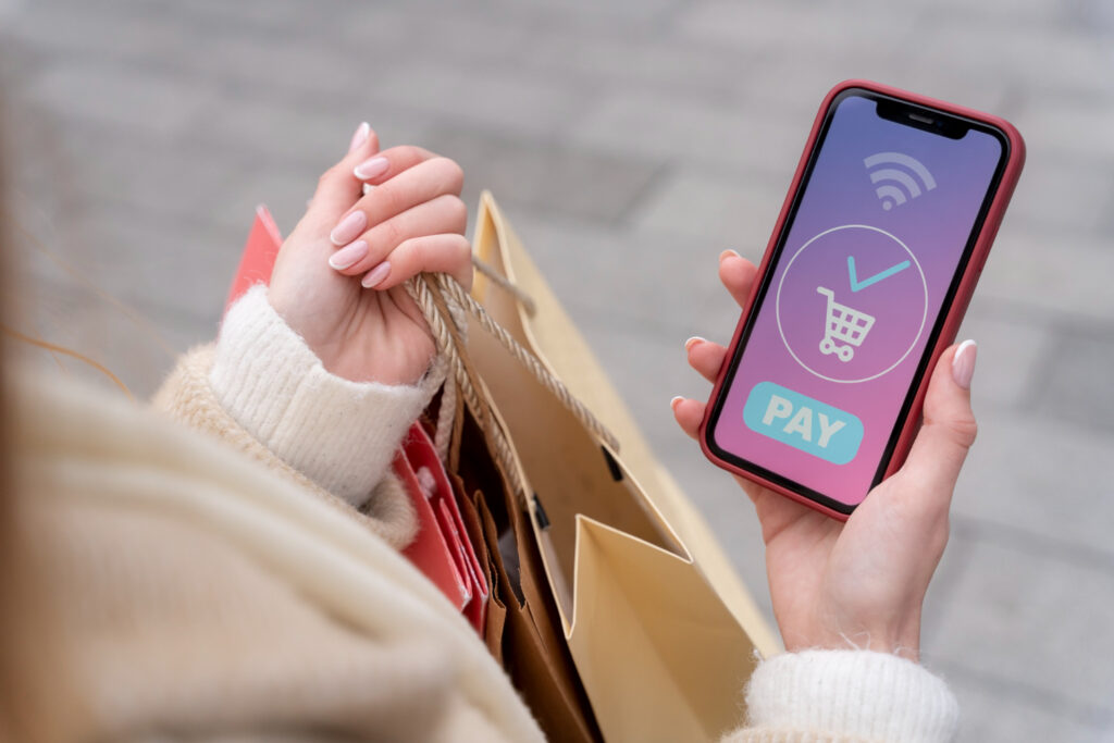 Una persona sostiene en una mano bolsas de compra y en otra un teléfono celular que muestra en la pantalla un pago satisfactorio.