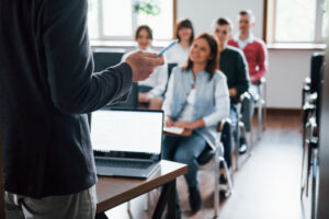 Vista de un salón de clases, con personas adultas sentadas en butacas, donde se imparte un curso de capacitación.