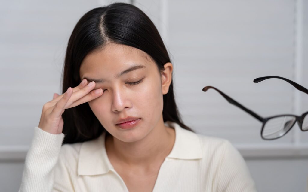 Mujer descansando sus ojos después de estar trabajando en su computadora ubicada cerca de una fuente de luz natural para evitar complicaciones por luz azul.
