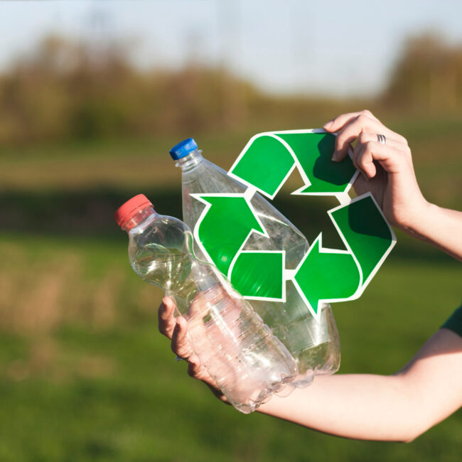 Dos manos sostienen envases de PET y un símbolo de reciclaje. De fondo se ve un paisaje de campo.